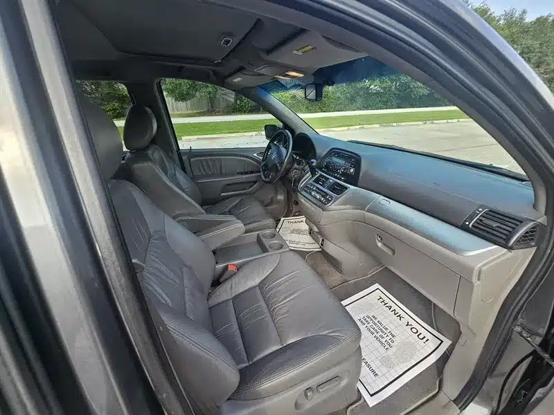 Side interior view of a used 2010 Honda Odyssey EX-L showing second and third-row seating with gray leather upholstery, for sale in Spring, TX.
